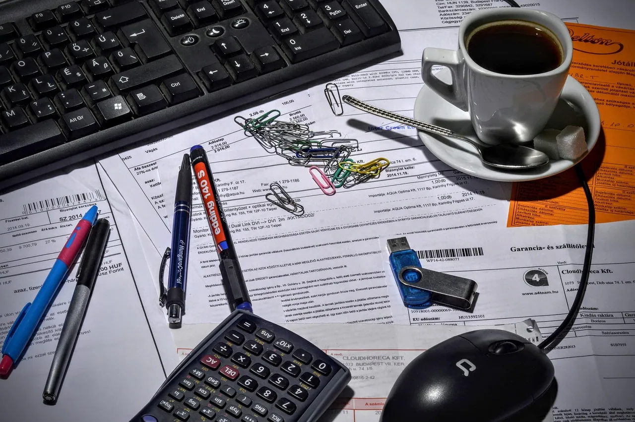 A desk with a calculator, documents and a coffee.